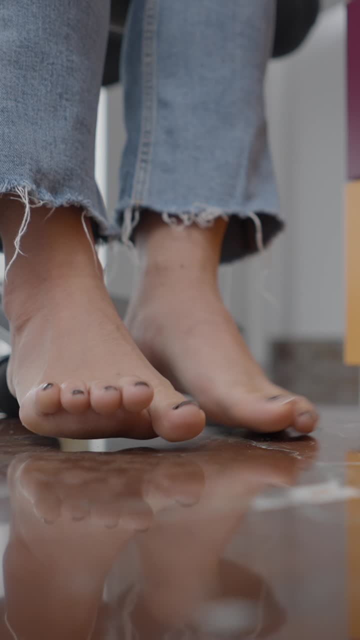 Piedi con smalto scuro e jeans su pavimento riflettente
