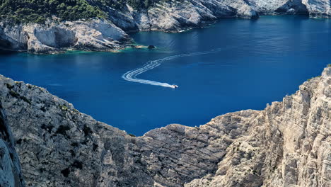 Looking-down-a-stony-mountain,-watching-a-boat-passing-on-the-blue-water-of-the-Navagio-Island,-Greece,-static-shot