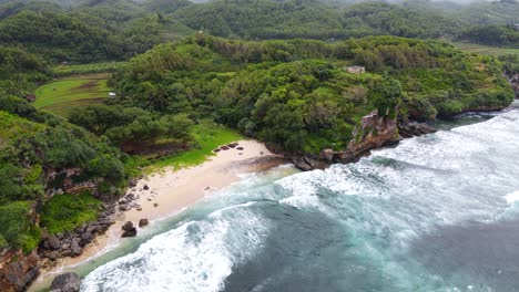 Aerial-view-of-whitecap-waves-crashing-onto-tropical-beach-and-coastline-cliffs,-Indonesia
