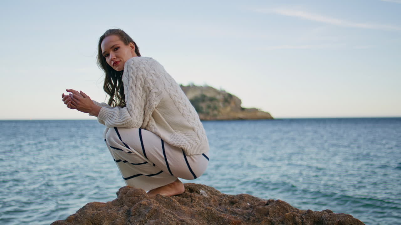 Romantic woman contemplating sea horizon crouching on beach rocks