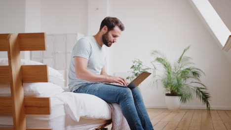 Junger-Mann-Sitzt-Auf-Dem-Bett-In-Der-Loft-Wohnung-Und-Arbeitet-Am-Laptop