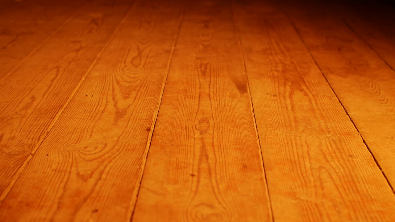 Close-up of a worn wooden floor with rich textures and warm orange tones