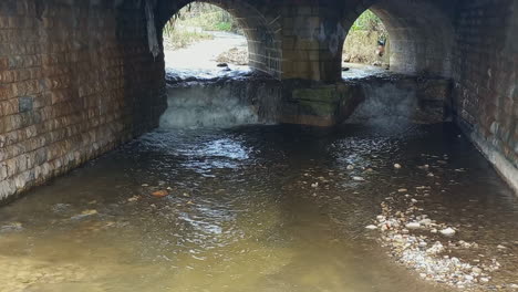 stone bridge with two arched exits through which the running water of the stream passes