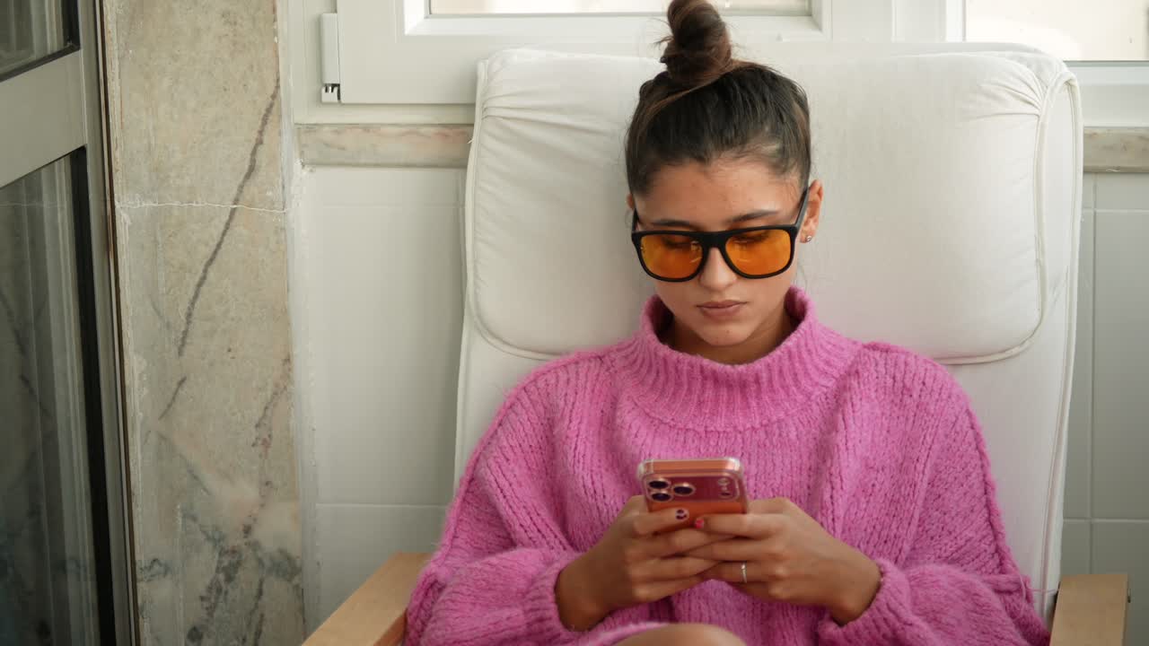 Giovane donna che usa lo smartphone mentre è seduta su una poltrona