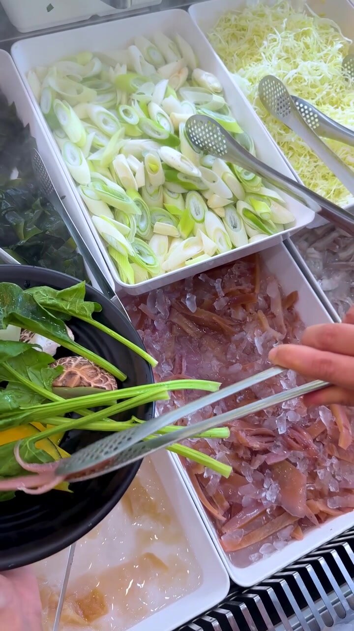 En person bruger metaltænger til at samle syltet blæksprutte op fra en isafkølet buffet.