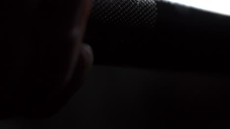 mano alrededor de la barra de levantamiento de pesas en el gimnasio iluminado oscuro
