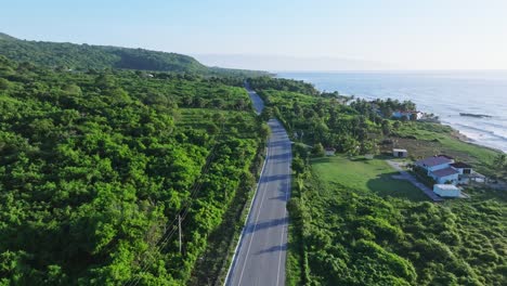 aerial flyover empty barahona coastal road surrounded by green landscape and caribbean sea at sunrise