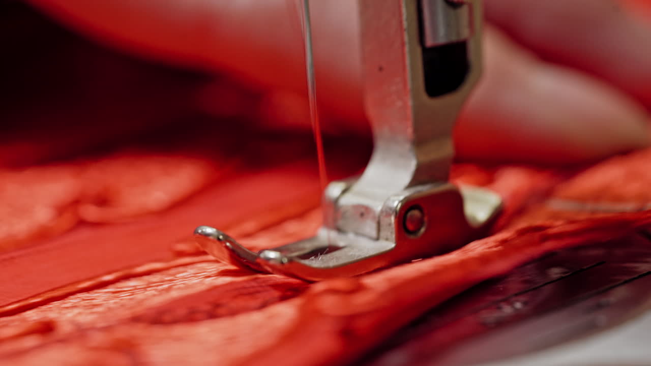 Steel part of sewing machine with a needle working on red cloth. Seamstress woman is sewing on modern machine with red fabric. Close-up