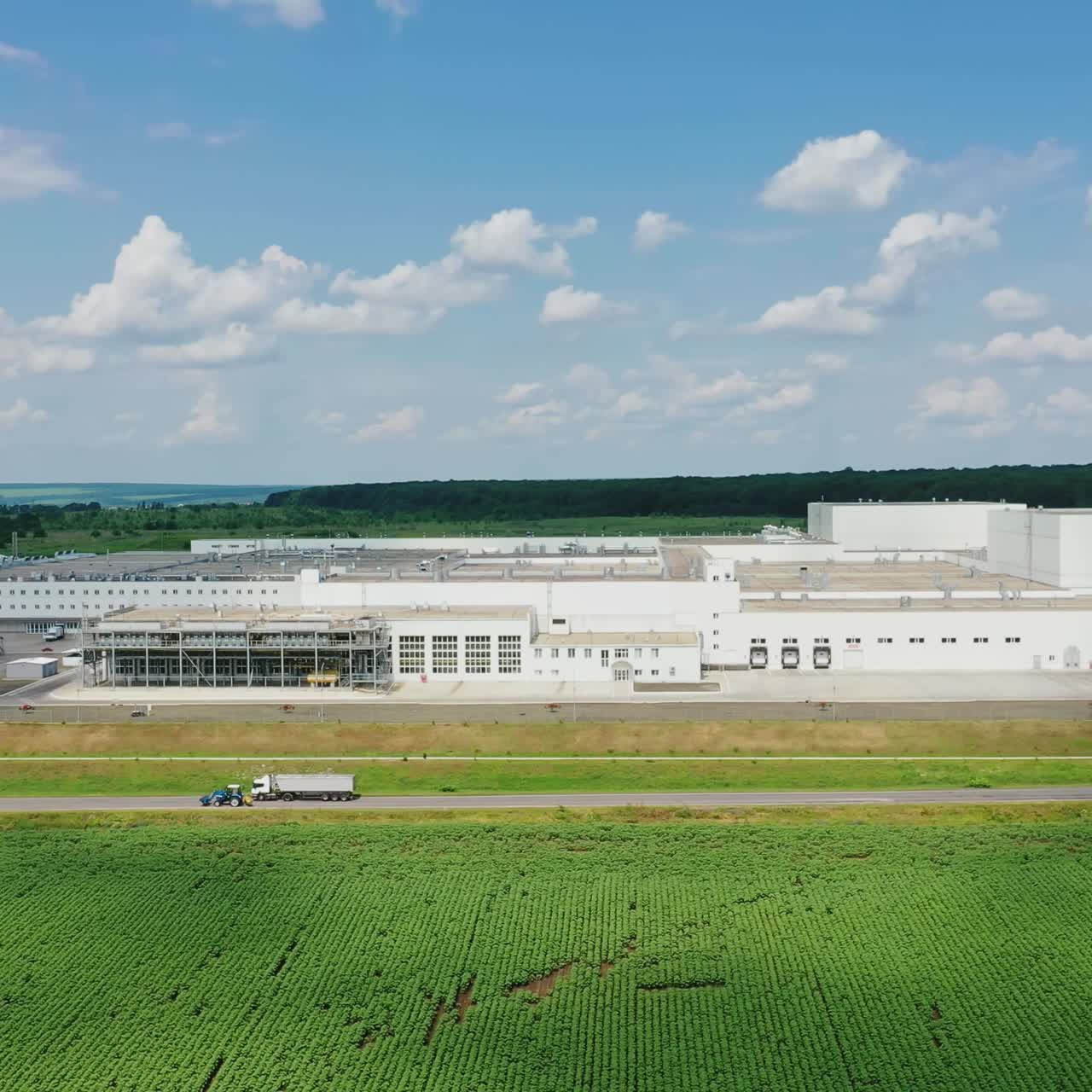 Modern industrial complex on green field. Large territory of manufacture near the road with cars on beautiful nature background. Drone view.