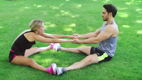 Happy-couple-man-and-woman-doing-stretching-exercise-on-grass-in-summer-park
