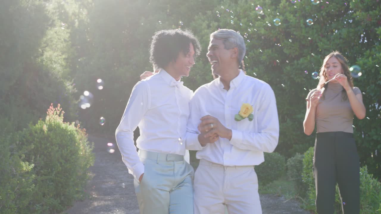 Mangfoldig gruppe går på havesti og blæser sæbebobler, to mænd holder hænder, læner sig, fejrer.
