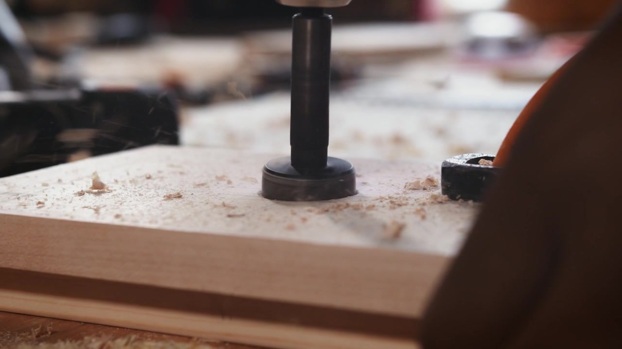 Close-up van een Forstnerboor die een houten plank boort op een kolomboormachine, waarbij een gat met platte bodem ontstaat terwijl houtspaanders zich verzamelen tijdens het houtbewerkingsproces