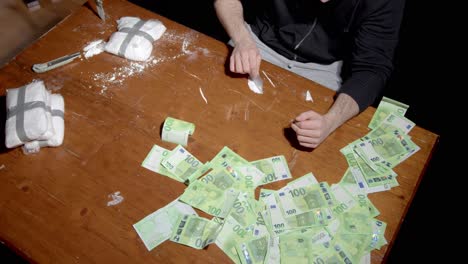 wealthy european man forming lines of cocaine powder on the table with scattered dirty money