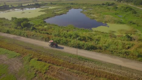 Drohnenaufnahme-Eines-Traktors,-Der-Auf-Einer-Unbefestigten-Straße-Durch-Die-Landschaft-Fährt