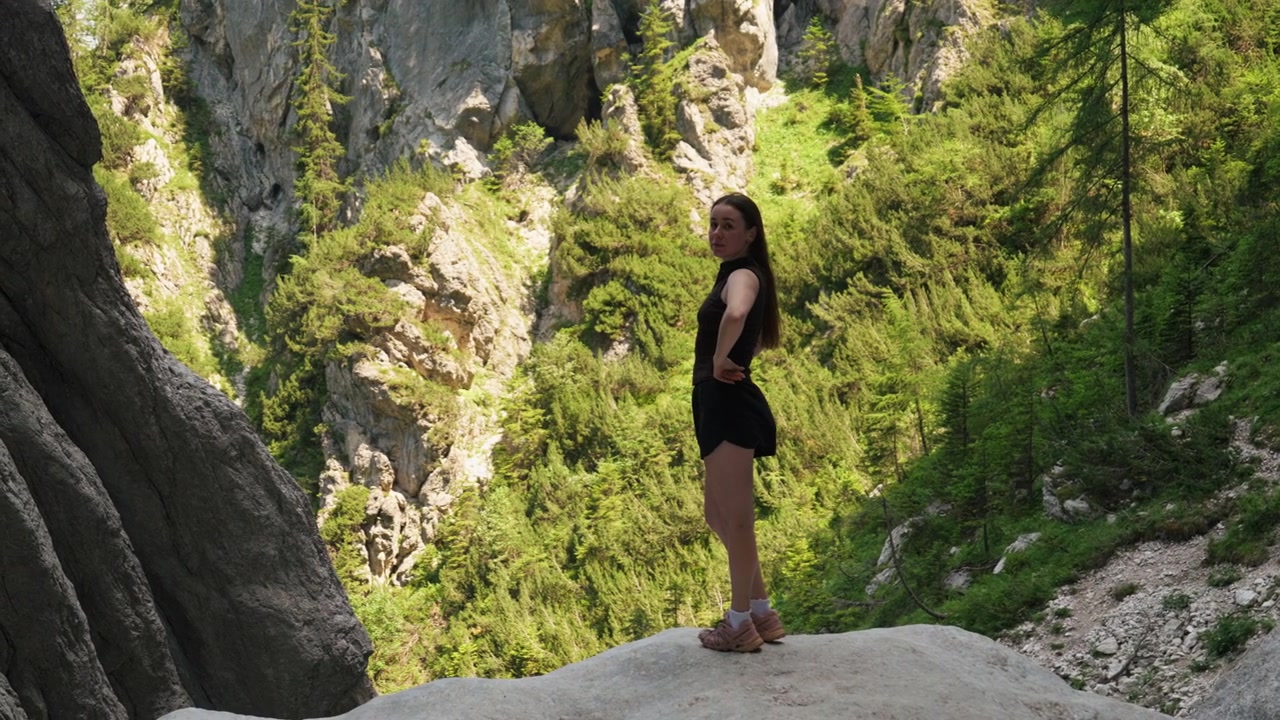 Mulher caminhante está em uma grande rocha com vista para uma floresta verde de montanha e penhascos acidentados. Cena ao ar livre mostrando caminhada, aventura, fitness e exploração