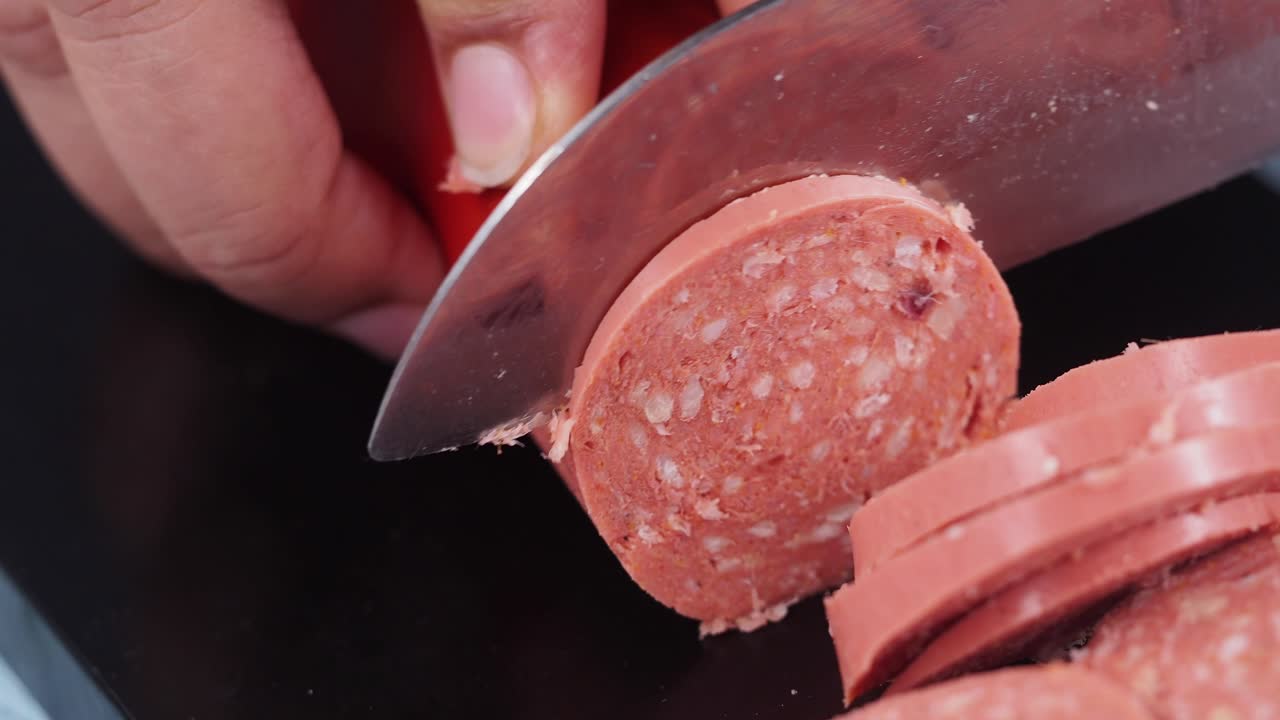 Primo piano di mani che tagliano una salsiccia con un coltello su un tagliere