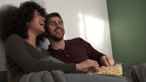 cheerful couple enjoying popcorn and movie at home