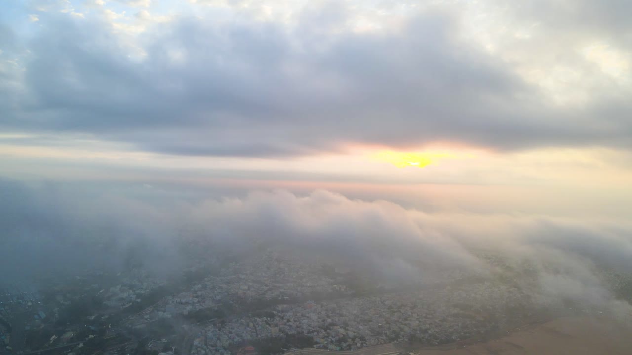 Aerial drone shot capturing the serene beauty of Vijayawada in the early hours, with sunlight breaking through the clouds.