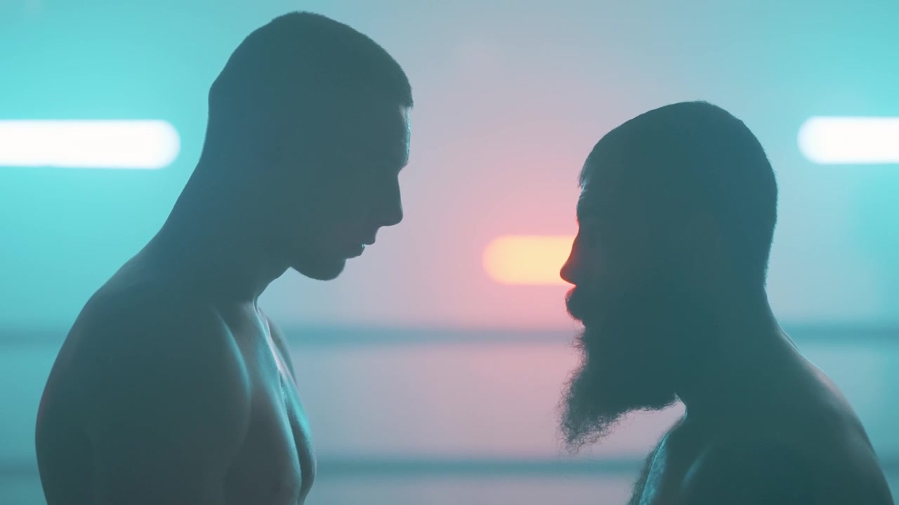 Due pugili maschi si affrontano in un ring da boxe illuminato al neon.