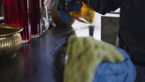 sección media de una persona que usa guantes y un delantal desinfectando la barra en una cafetería