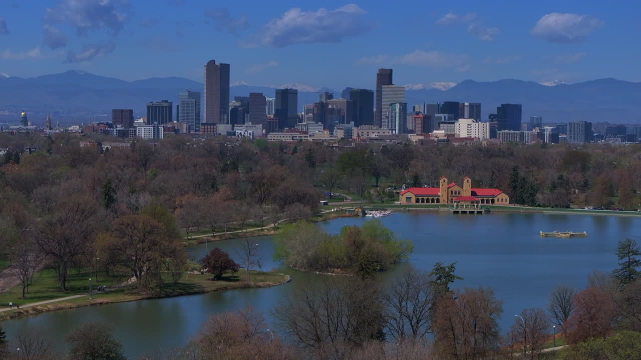 City Park Denver Colorado Lake Pavilion vibrant blossom spring summer aerial drone sunny blue sky snow capped Rocky Mountains front range cityscape green lush grass trees upwards motion