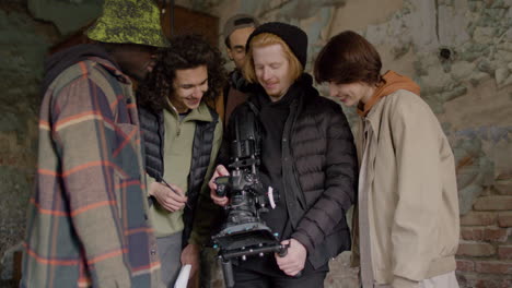 el equipo de producción y el camarógrafo se ríen mientras revisan una escena en una cámara en un edificio en ruinas