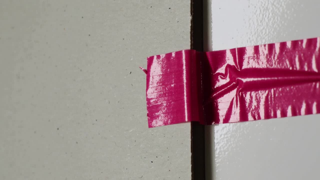 Cámara desplazándose hacia abajo y a la derecha, revelando cinta rosa que une la costura de una puerta, mostrando arrugas.