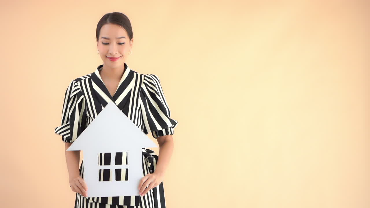 A young conservatively dressed woman holds a cutout of a house out in front of her. Copy space