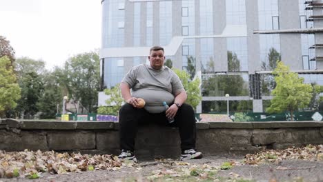 portrait of an overweight man sitting outside eating a bun and drinking water portrait of an overweight man sitting outside eating a bun and drinking water a fat man on the background of a building in the city