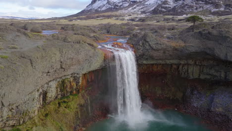 Salto del Agrio near Caviahue, Neuquén, shows a powerful waterfall surging over columnar basalt into a teal pool, hurling spray and mist as a river thunders through the volcanic canyon, Drone orbiting