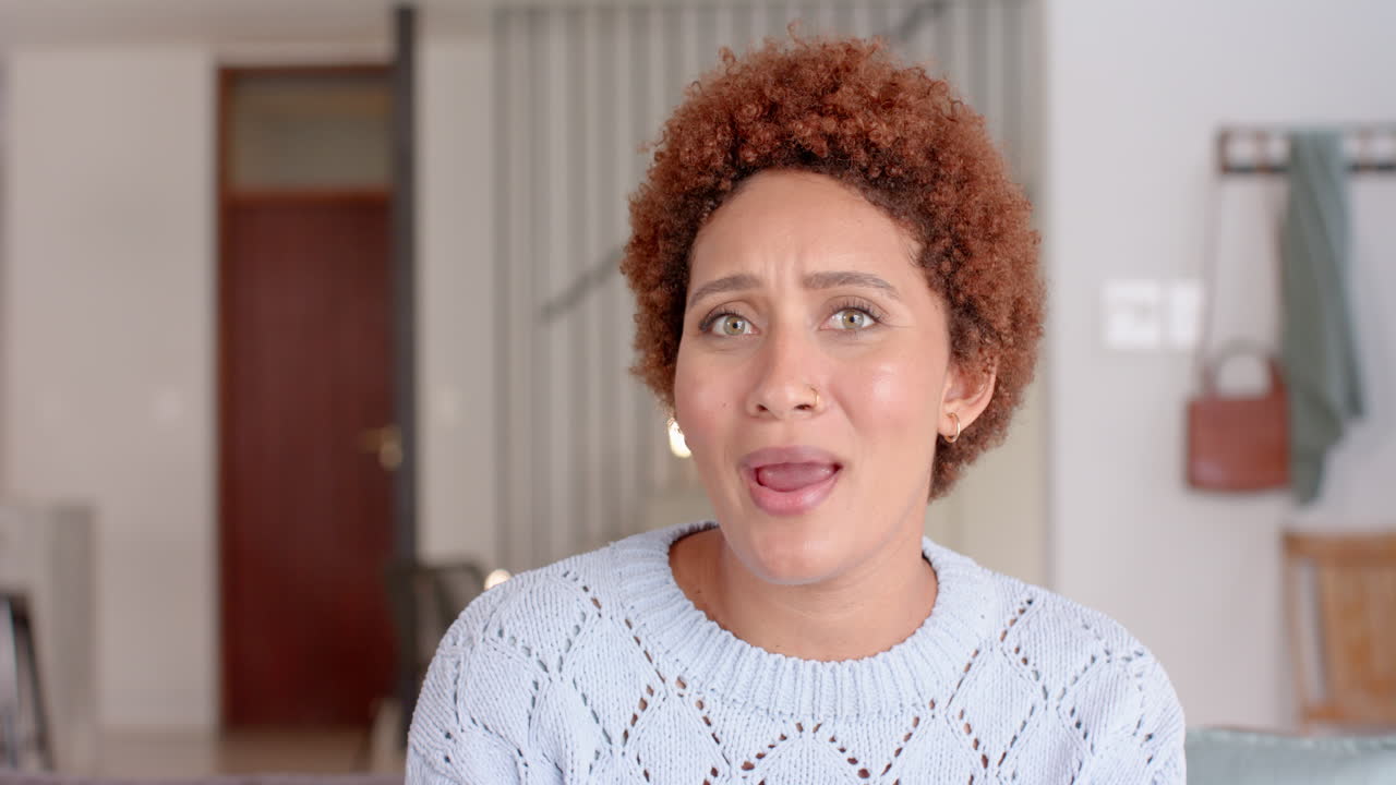 Expressing surprise, woman with curly hair gesturing with hand indoors, video call