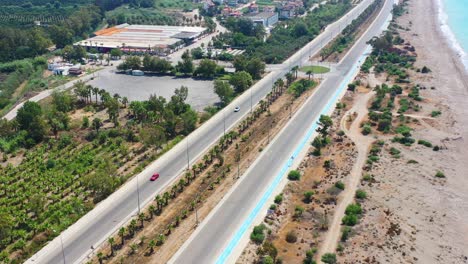 Vista-Aérea-De-Una-Carretera-Costera-Vacía-En-Finike-Turquía-En-Un-Día-Soleado-De-Verano-Con-Una-Playa-De-Arena-Y-Palmeras