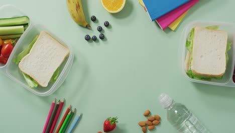 Video-of-healthy-packed-lunch-of-fruit-and-vegetables,-with-coloured-pencils-and-notebooks