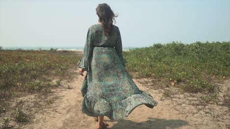 Brunette-woman-walking-slow-motion-sandy-beach-path-with-beautiful-flowing-dress-in-wind