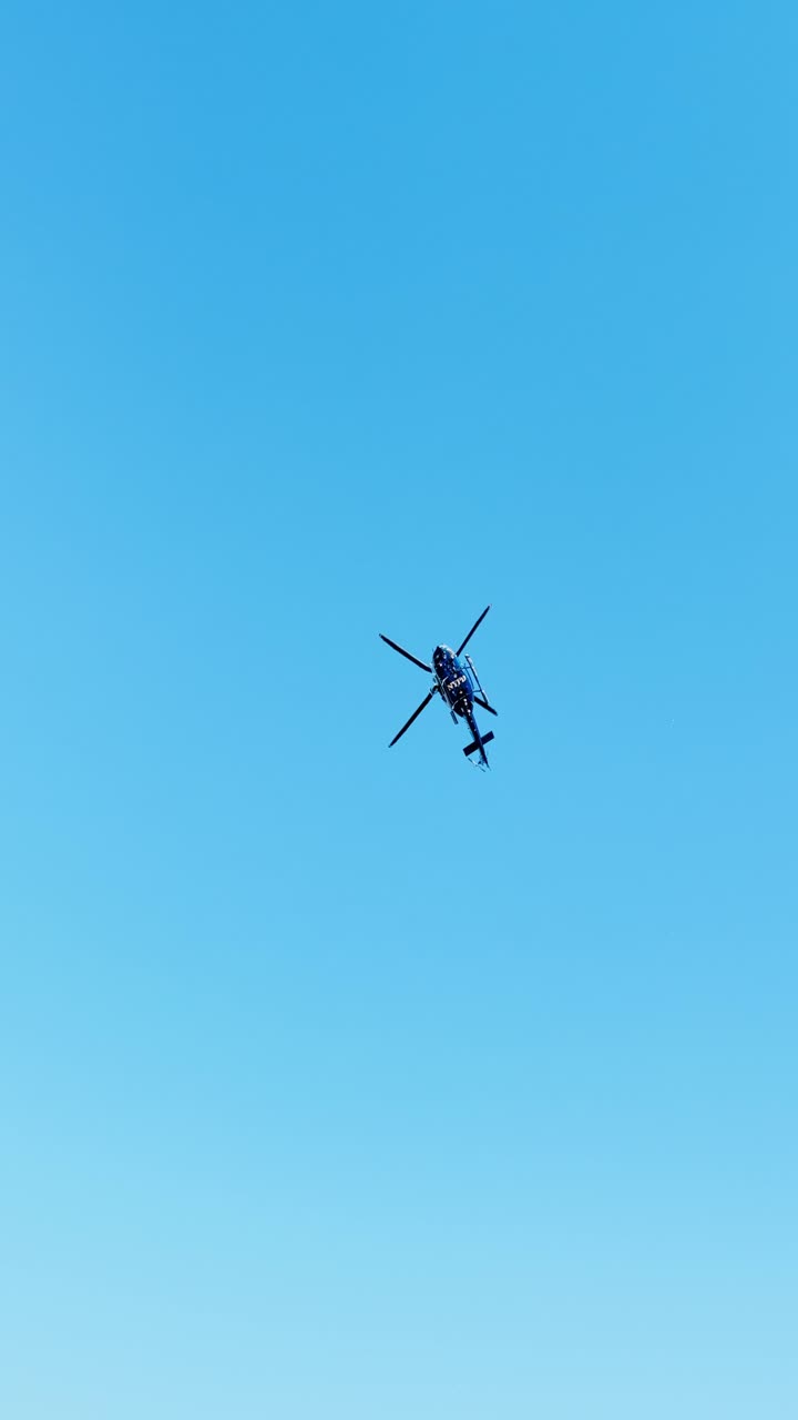 Politihelikopter i luften mod klar himmel. Enkelt helikopter med roterende rotorer fotograferet nedefra mod en ensfarvet blå baggrund.