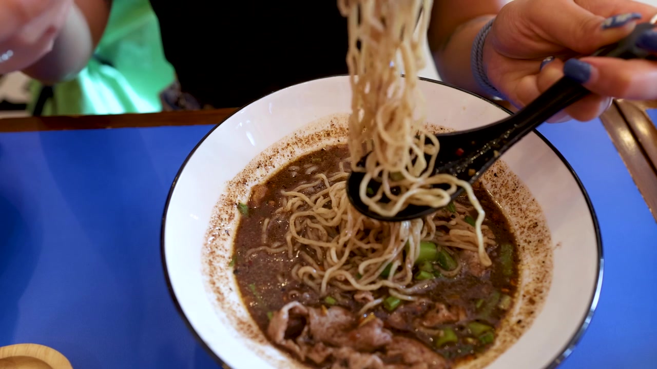 Primo piano di mani che mangiano zuppa di noodle con bacchette e cucchiaio