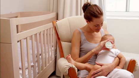 Beautiful-brunette-sitting-in-rocking-chair-feeding-her-baby-daughter