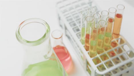 Coloured-liquids-in-flasks-with-test-tubes-in-stand-on-white-background,-slow-motion