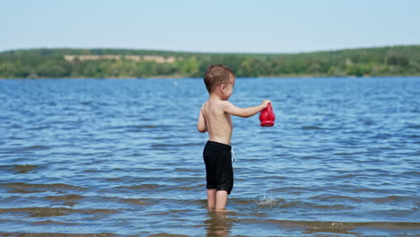 child playing in the lake with a red bucket