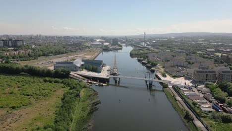 aerial lower and tilt down over the river clyde, riverside museum and govan footbridge with glasgow city skyline in distance, glasgow, scotland, uk
