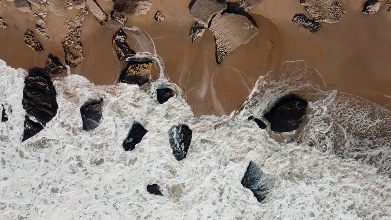 Veduta aerea a volo d'uccello di onde oceaniche che si infrangono su una spiaggia rocciosa a Nazaré, Portogallo