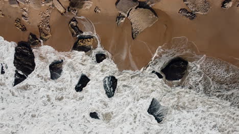 una imagen aérea de las olas del océano que se estrellan en la playa rocosa de nazare, portugal