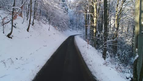 Drone-flying-low-above-the-road-in-forest-covered-with-snow