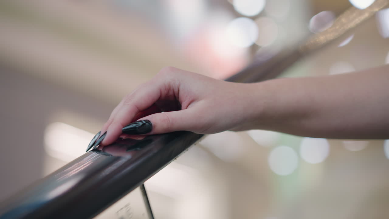 긴 검은색 은 손을 가진 여자의 손이 올라가는 동안 에스컬레이터 레일에 누워있는 클로즈업, 멋진 반사와 함께 현대적인 실내 설정에서 부드러운 보케 조명을 특징으로하는 배경