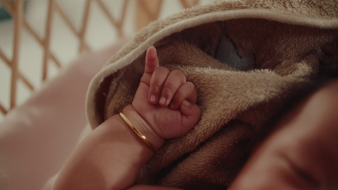 Newborn baby infant arm hand cute close up while resting in a wooden cradle box in warm natural light wearing golden bracelet