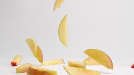 sliced red and yellow fuji apple pieces falling onto white table top and bouncing into a pile in slow motion