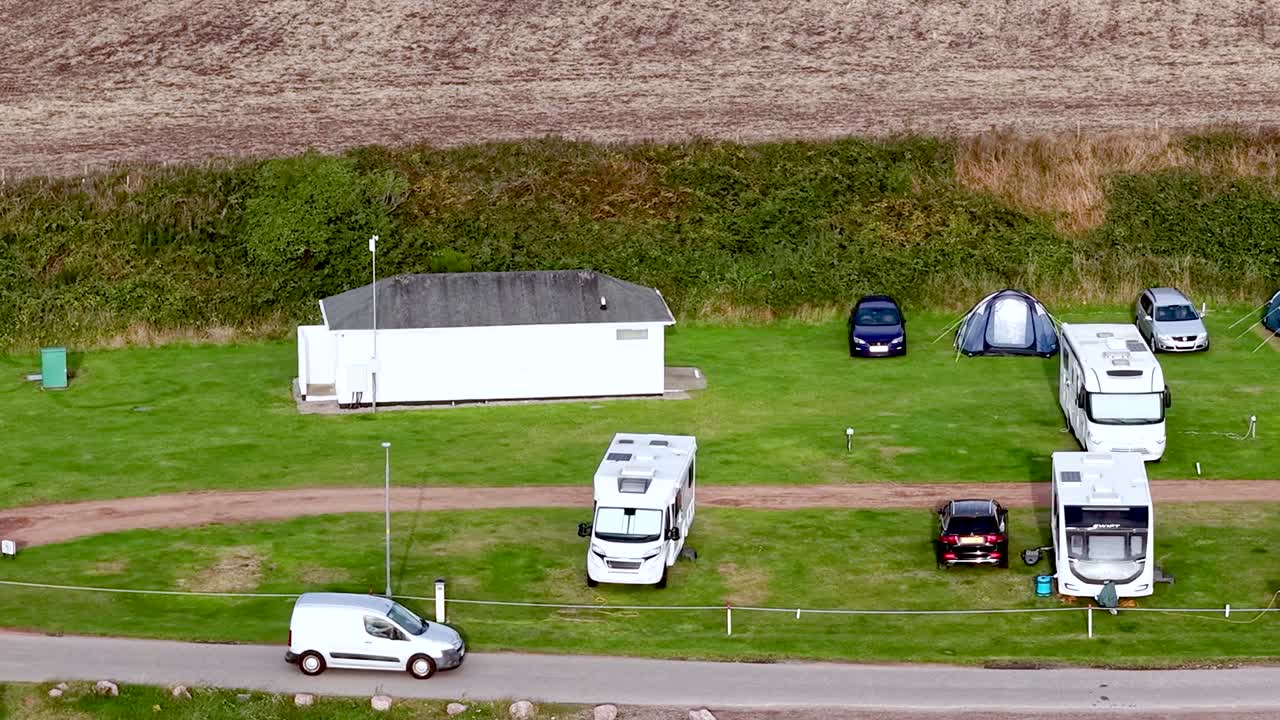 Кадры с дрона показывают автодома и палатки, припаркованные на зеленом поле возле здания.