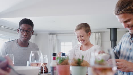 Group-Of-Young-Friends-Sitting-Around-Table-At-Home-Enjoying-Meal-Together