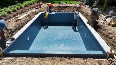 a team of workers is busy installing a swimming pool in a suburban backyard. they carefully work on the structure, ensuring precise placement and preparation for filling.