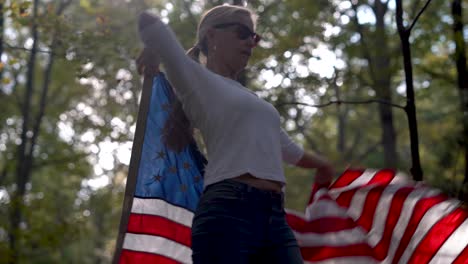 primer plano de una mujer rubia bonita retroiluminada en un bosque bailando con una bandera americana